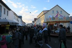 Allerheiligenmarkt Hungen, Marktreiben in der Kaiserstraße Menschen flanieren durch eine Straße mit Buden an beiden Seiten und einem Karussell rechts. Im Hintergrund das Rathaus von Hungen.