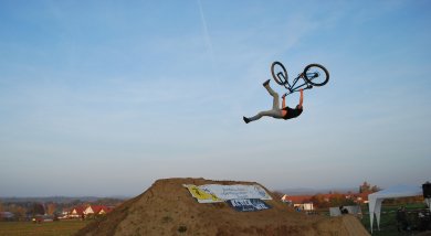 Ein Biker vollführt hoch über der Schanze einen Salto mit seinem Bike 