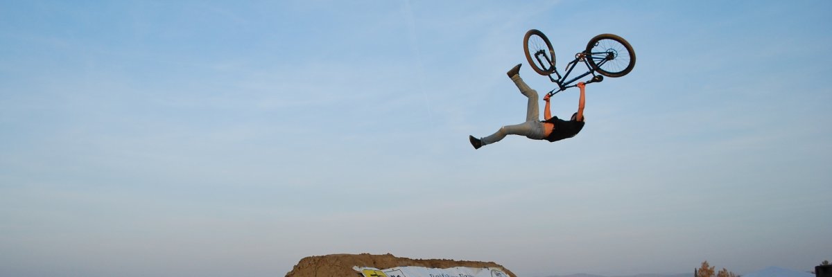 Ein Biker vollführt hoch über der Schanze einen Salto mit seinem Bike 