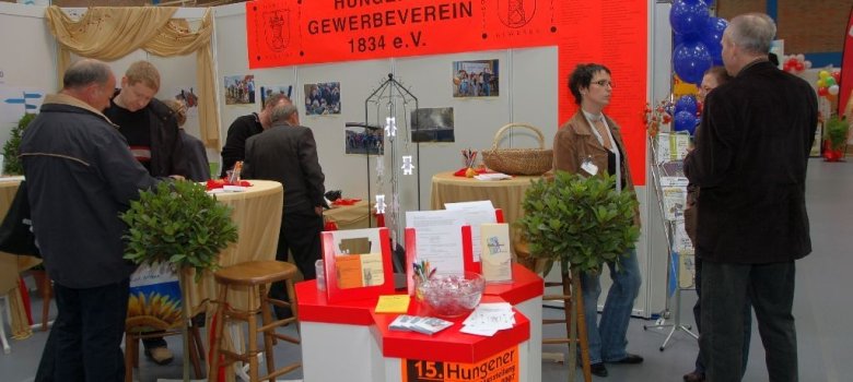 Ausstellungsfläche mit Tischen, Postern und einigen Menschen im Gespräch vertieft