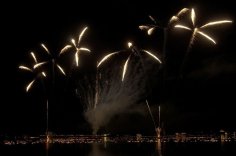 Feuerwerk über dem See mit beleuchtetem Ufer bei Nacht