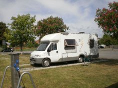 Wohnmobil auf Stellplatz unter rot blühenden Kastanien mit Versorgungssäule links