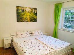 weiße Holzmöbel und Blick durchs Fenster ins Grüne im Schlafzimmer in der "Zeitraumwohnung"