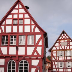 Zwei Fachwerkhäuser mit rotem Fachwerk. Links das alte Rathaus mit Rundbogenfenstern im Erdgeschoss, rechts Giebelseite des Wohnhauses eines Fachwerkgehöfts.