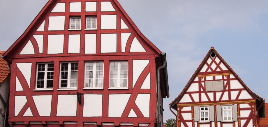 Zwei Fachwerkhäuser mit rotem Fachwerk. Links das alte Rathaus mit Rundbogenfenstern im Erdgeschoss, rechts Giebelseite des Wohnhauses eines Fachwerkgehöfts.
