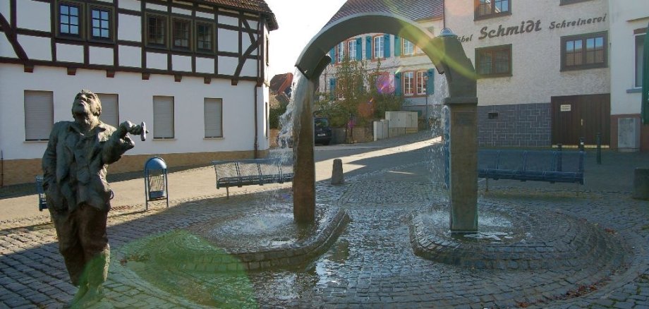 Hungen Marktplatzbrunnen mit Heiner-Statue, durch den Brunnebogen sieht man das Pfarrhaus